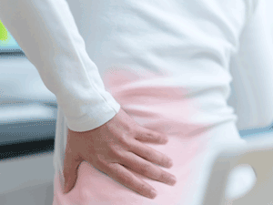 A woman with lower back pain clutches her left back with her hand.